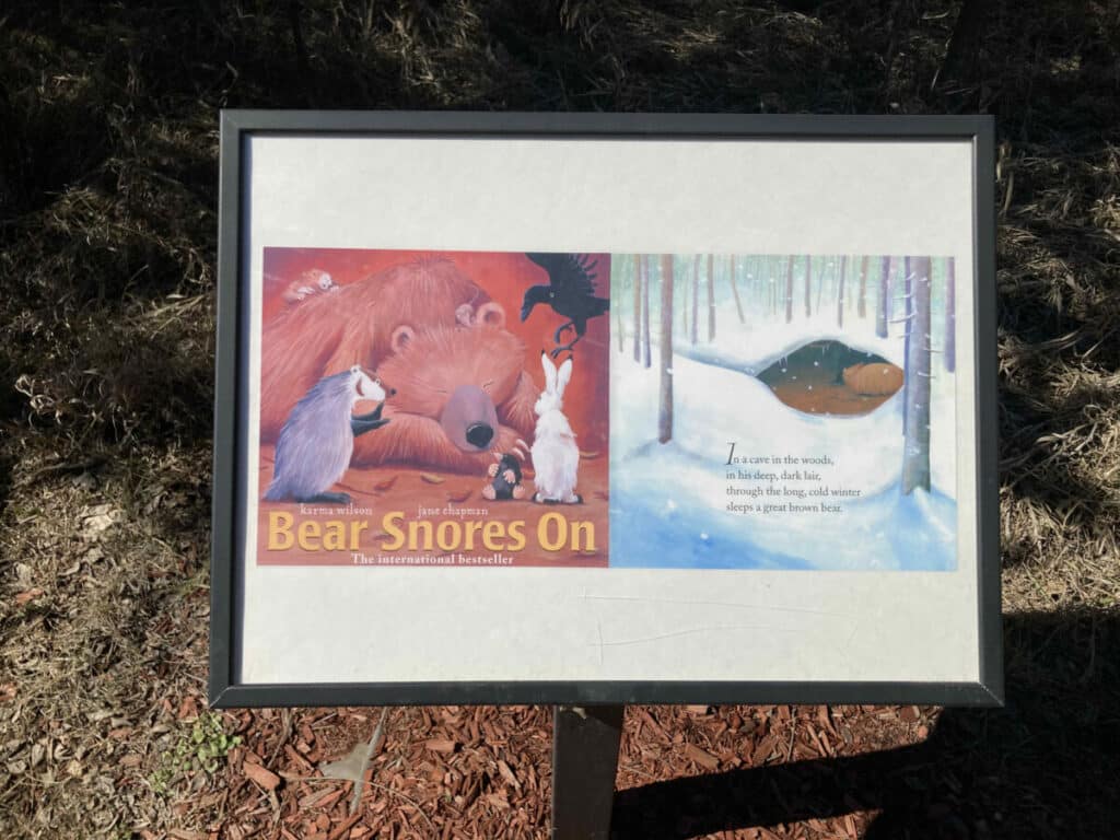 An outdoor StoryWalk sign holding the cover and first page of the book "Bear Snores On"