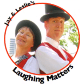 "Jay & Leslie's Laughing Matters" with two performers standing back-to-back and wearing black hats, white shirts and red vests.