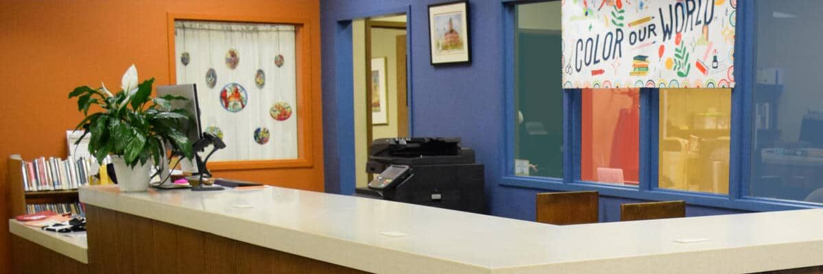 Library circulation desk with a "Color Our World" summer reading poster behind it